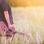 A man holding a guitar in a field.