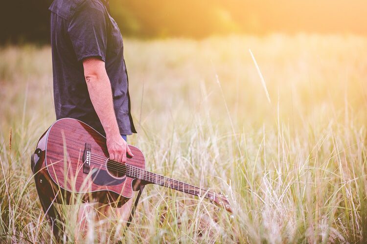 A man holding a guitar in a field.